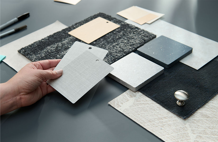 Hand holding samples of laminate above other samples of fabric and carpet in gray, black and cream tones