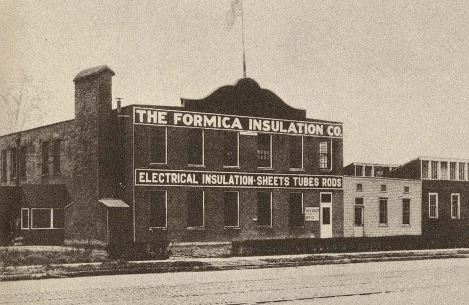 A historic, black and white image of a brick factory with the name 'The Formica Insulation Co.' on the top of the building