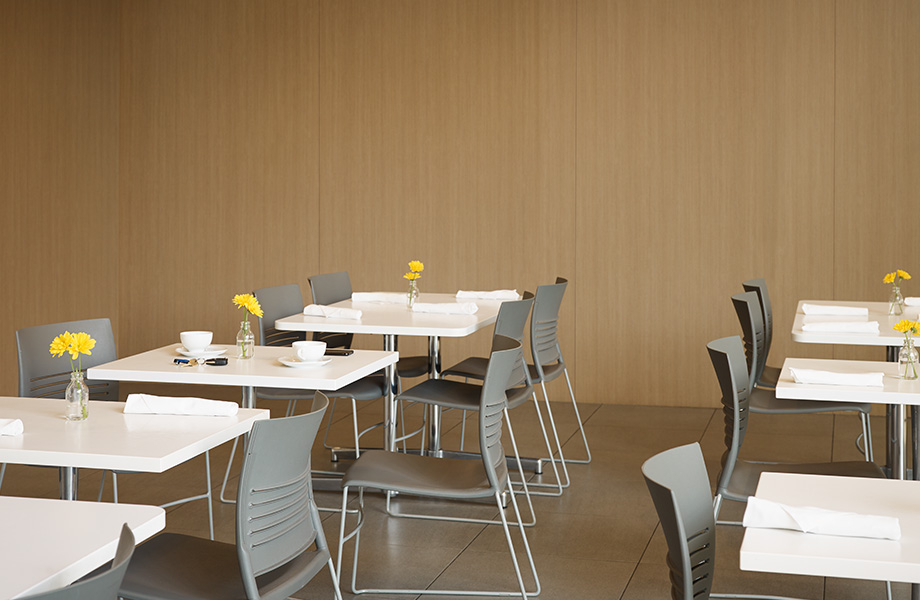 Restaurant with wood-paneled walls in Pecan Woodline Formica Laminate and white tables in Arctic Everform Solid Surface with gray chairs